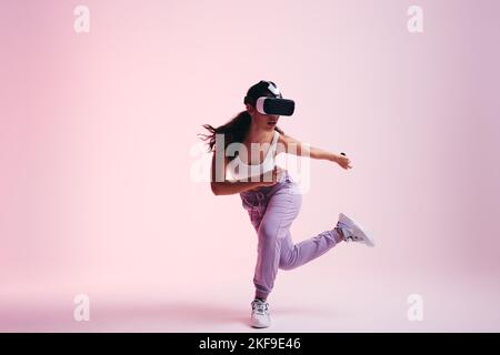 Woman exploring the metaverse. Active young woman gaming with virtual reality goggles and controllers. Energetic young woman having a 3D experience in Stock Photo