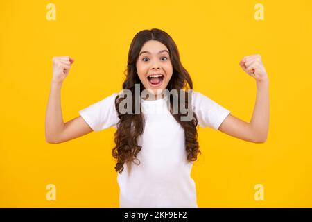 Teenager child overjoyed successful do winner gesture clench fist say yes isolated on yellow background studio. Excited teen girl. Stock Photo