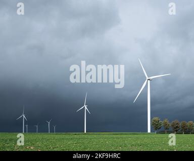 dark threatening grey sky and white wind turbines in belgium Stock Photo