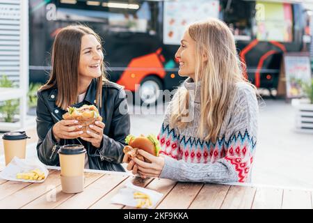 Two middle-aged women eat fast food and chat at a street food market. Stock Photo