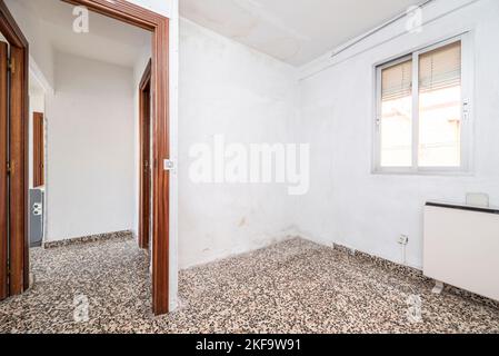 Empty living room with glossy gray terrazzo flooring with white painted walls, reddish door joinery and window with roller shutters Stock Photo