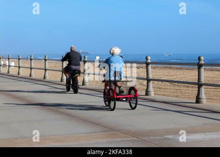 A senior couple riding hire bikes along the boardwalk, Virginia Beach Oceanfront, from near 36th Street. Stock Photo