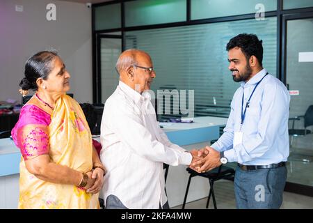 Happy smiling banker greeting by shaking hand of elderly couple at bank - concept of financial support, banking adviser and consultation. Stock Photo