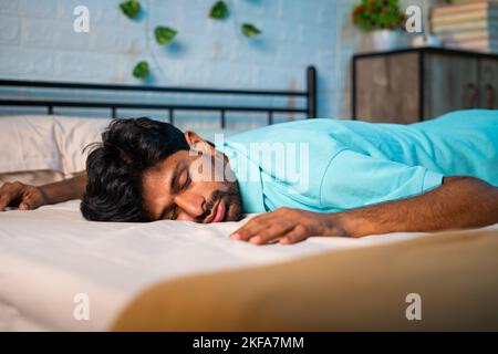 Tiered exhausted young man fallen on bed at bedroom - concept of fatigue, overworked and sleeplessness Stock Photo