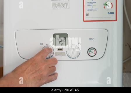 Man's hand turning down the dial on a boiler unit heating system. Stock Photo