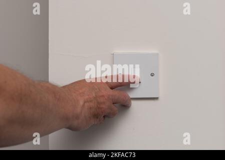 Picture of man's hand turning off the light switch to save energy. Cost of living crisis in the UK. Stock Photo