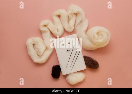 toy needle felting kit with white wool on pink table. small woolen handmade product with foam sponge Stock Photo