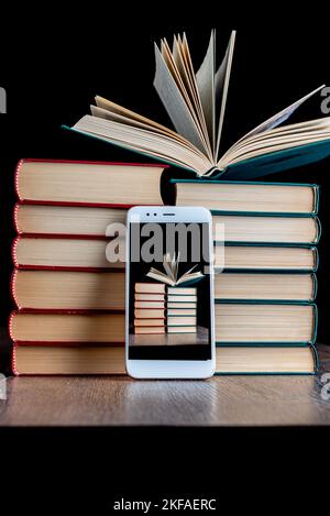 Stack of books with an open book and a smartphone. On the smartphone screen, a stack of books with an open book. Copy space. Stock Photo