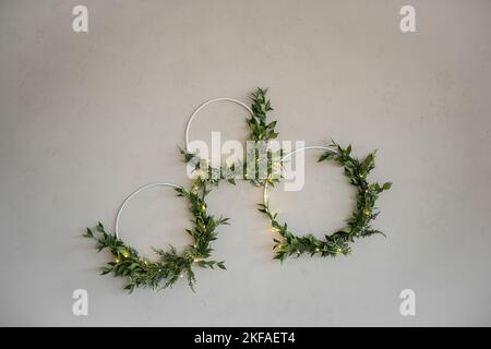 On gray concrete wall, there are three laconic, elegant, green wreaths made from natural materials. Festive garland. Minimalist interior decor in rust Stock Photo