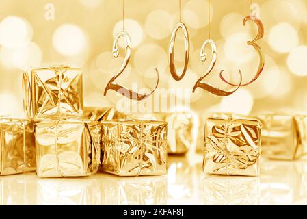 2023, new year card. Small Christmas gifts in shiny golden paper, bokeh lights background Stock Photo