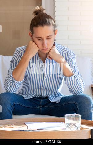 Vertical view of young man sitting in the sofa of the living room thoughtful while looking and reading at document on the wooden table Stock Photo