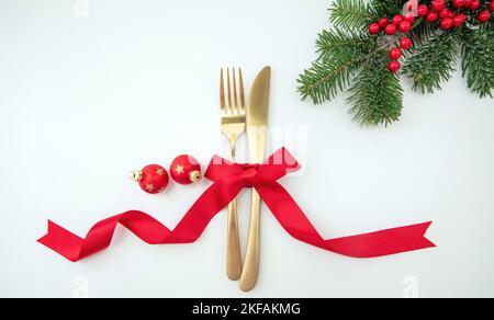 Christmas holiday celebration dinner. New Year table setting. Golden cutlery, Xmas decoration and red ribbon top view. Stock Photo