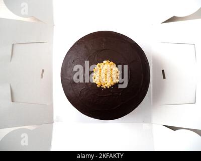 Vegan Chocolate Cake with Peanut Butter Filling, Covered with Chocolate Cream and Decorated with Small Pieces of Peanuts in a Open White Box Stock Photo