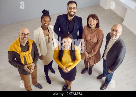 Team of happy multiracial business people standing in office, looking up and smiling Stock Photo