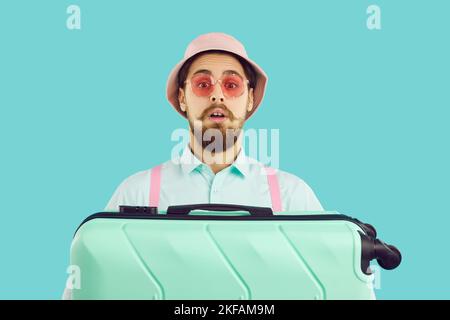 Young traveler holding his suitcase and looking at camera with funny surprised face expression Stock Photo
