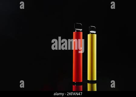 Two disposable e-cigarettes on a dark background. Electronic vape, an alternative to smoking cigarettes. Stock Photo