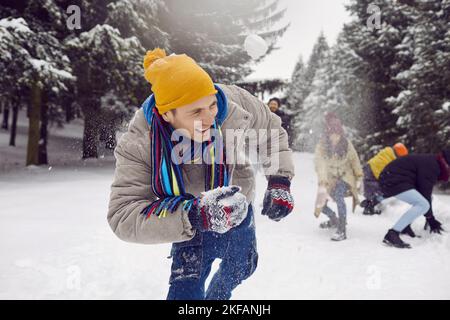 Young cheerful man laughing out loud while playing snowballs with friends in snowy forest. Stock Photo