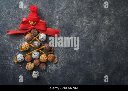 Christmas tree made of chocolate truffles, hazelnuts, anise stars, decorations, spoons and powdered sugar snow on dark background. Christmas holiday c Stock Photo
