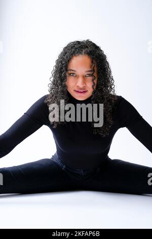 Young Multiracial Woman Doing the Splits on a White Background Looking Intensely at the Camera Stock Photo