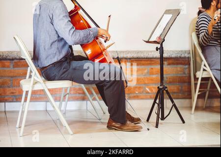 A musician playing cello with musical notes on the book notation stand in front of him Stock Photo