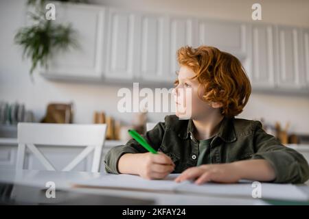 thoughtful redhead boy with pen doing homework and looking away Stock Photo