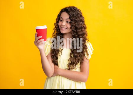 Teenage girl with take away cup of cappuccino coffee or tea. Child with takeaway cup on yellow background, morning drink beverage. Happy teenager Stock Photo