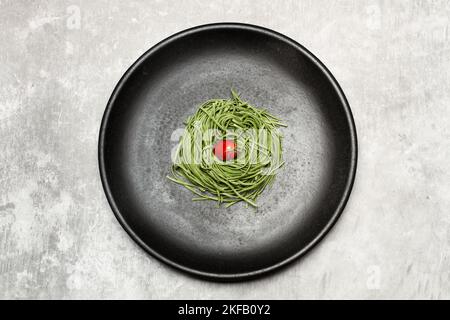 Vegetable spaghetti with a cherry tomato in a black plate in a top view Stock Photo
