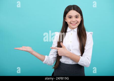 Look at advert. Teenager child points aside shows blank copy space for text promo idea presentation, poses against blue background. Stock Photo