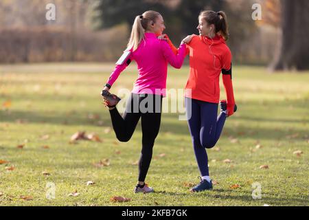Sporty female athletes are warming up before jogging, doing lower body stretching in the park. Stock Photo