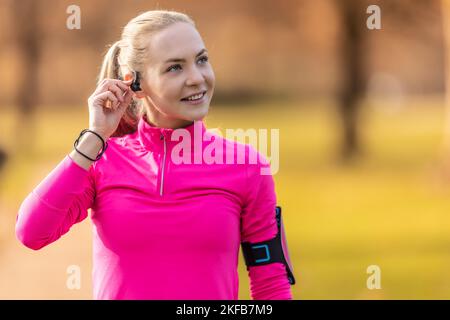 A beautiful young sportswoman listens to music through headphones with a mobile phone before running. Stock Photo