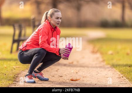 A resting sportswoman holds a plastic bottle with a drink in her hand after running in the park. Stock Photo