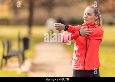 Young woman warming up before jogging, doing upper body stretching in the park. Stock Photo