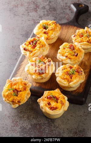 Freshly baked puff pastry cups stuffed with eggs, cheese and ham close-up on a wooden board on the table. Vertical Stock Photo