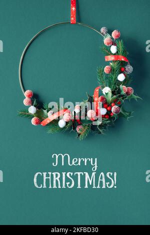 Christmas wreath with holly, fir twigs and frosted red berries. Flat lay, decorative border with greeting text Merry Christmas. Festive Xmas Stock Photo