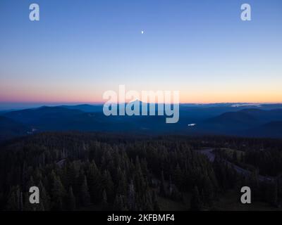Drone shot. Panoramic shot. Picturesque landscape. Coniferous forest, mountains and highway. The sky is colored with orange rays of the setting sun. B Stock Photo