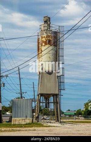 Old grungy rusty Silo for Concrete Batching Plant standing against blue cloudy sky with many electrical highlines near Cushing USA. Stock Photo