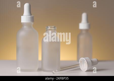 Three empty translucent glass dropper vials, one open, one blurry. Different-sized bottles on yellow background. Horizontal beauty mockup, copy space. Stock Photo