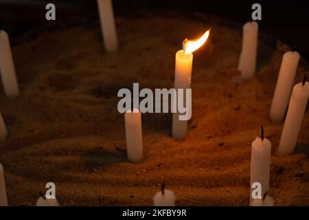 Goiânia, Goias, Brazil – November 12, 2022: Several candles in a sand holder in the church. One candle lit and other candles unlit. Candles. Stock Photo