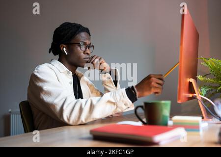 Serious focused African American man student looking attentively at monitor sits at office desk Stock Photo