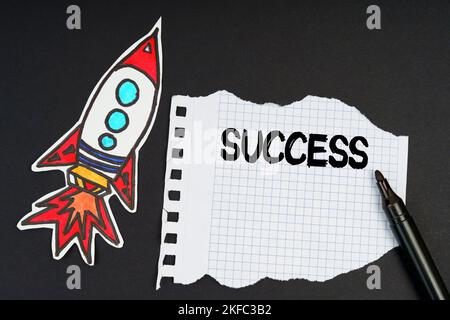 Business and finance concept. On a black background, a rocket, a marker and paper with the inscription - success Stock Photo