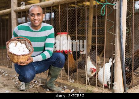 Smiling man holds a basket of chicken eggs in his hands. Stock Photo