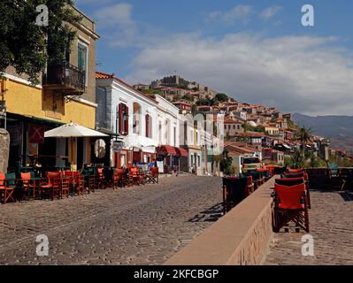 Molyvos street scene, with cafes and bars just above the harbour with Molyvos castle (Kastro) on top of the hill. Lesbos, Greece. October 2022. Autumn Stock Photo