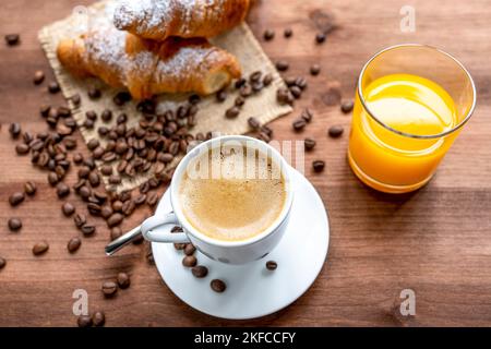 coffee, orange juice and croissants on a rustic wooden table decorated with coffee beans. Stock Photo