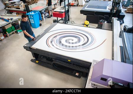 In the printing house, an experienced technician works on a UV printer. Production work. Check the print quality. Stock Photo