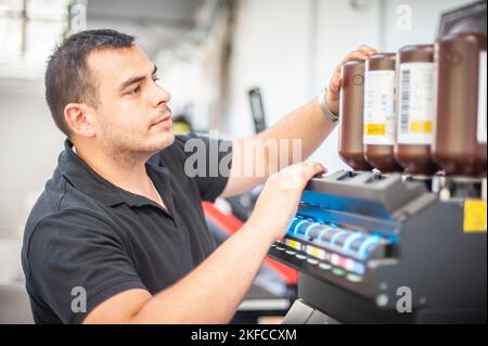 In the printing house, an experienced technician works on a UV printer. Production work. Check the print quality. Stock Photo