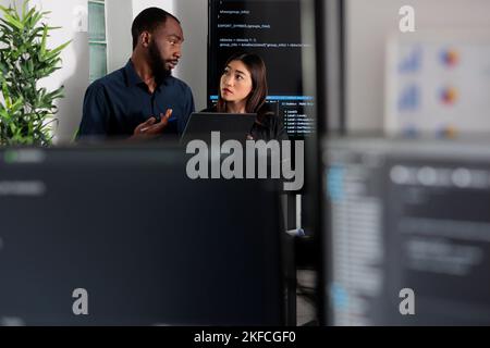 Diverse app programmers looking at algorithms artificial intelligence on laptop computer in digital software company. Developers discussing database script and firewall server, big data interface. Stock Photo
