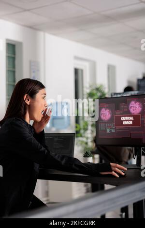 Software developer woman having web server hacked, looking at critical error on computer monitor in office. Asian programmer trying to solve hacking problem, firewall security. Stock Photo