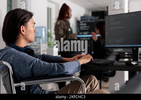 Disabled software developer typing programming code on computer, working with cloud computing terminal window. Software engineer in wheelchair writing html algorithm in it big data office Stock Photo