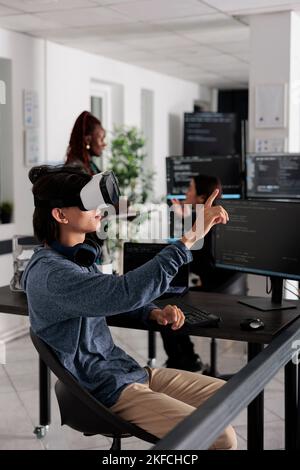 Software developer wearing virtual reality headset working to develop security program in it software company office, Big data admin with vr goggles coding html script with database. Stock Photo