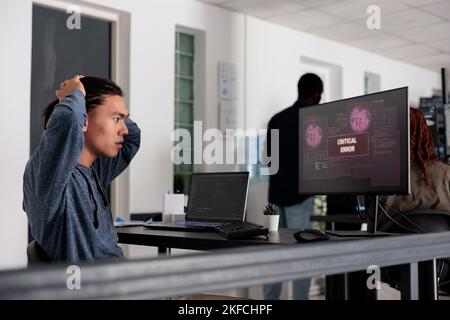 Nervous it programmer having security breach alert on computer display, trying to solve hacking in big data office, Programmer using terminal window and having system hacked crash. Stock Photo